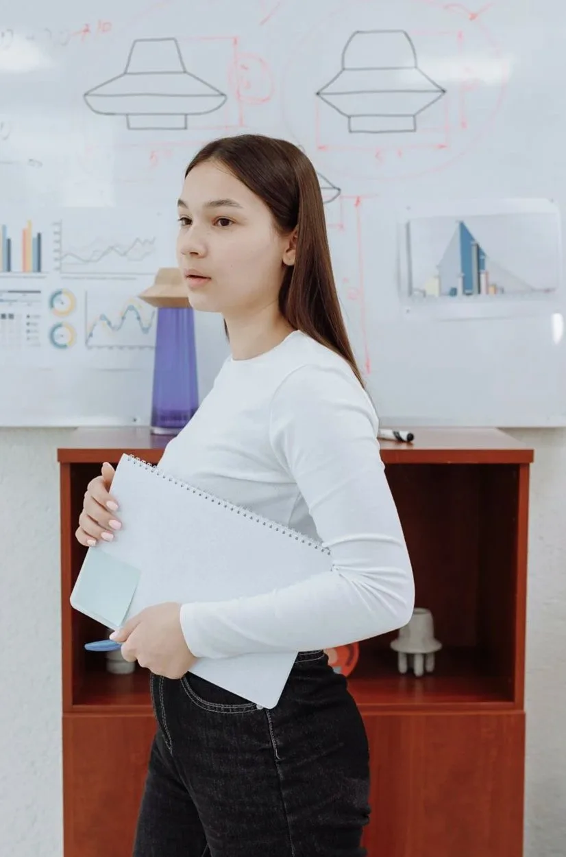 ホワイトボードの前で資料を手に立つ女性